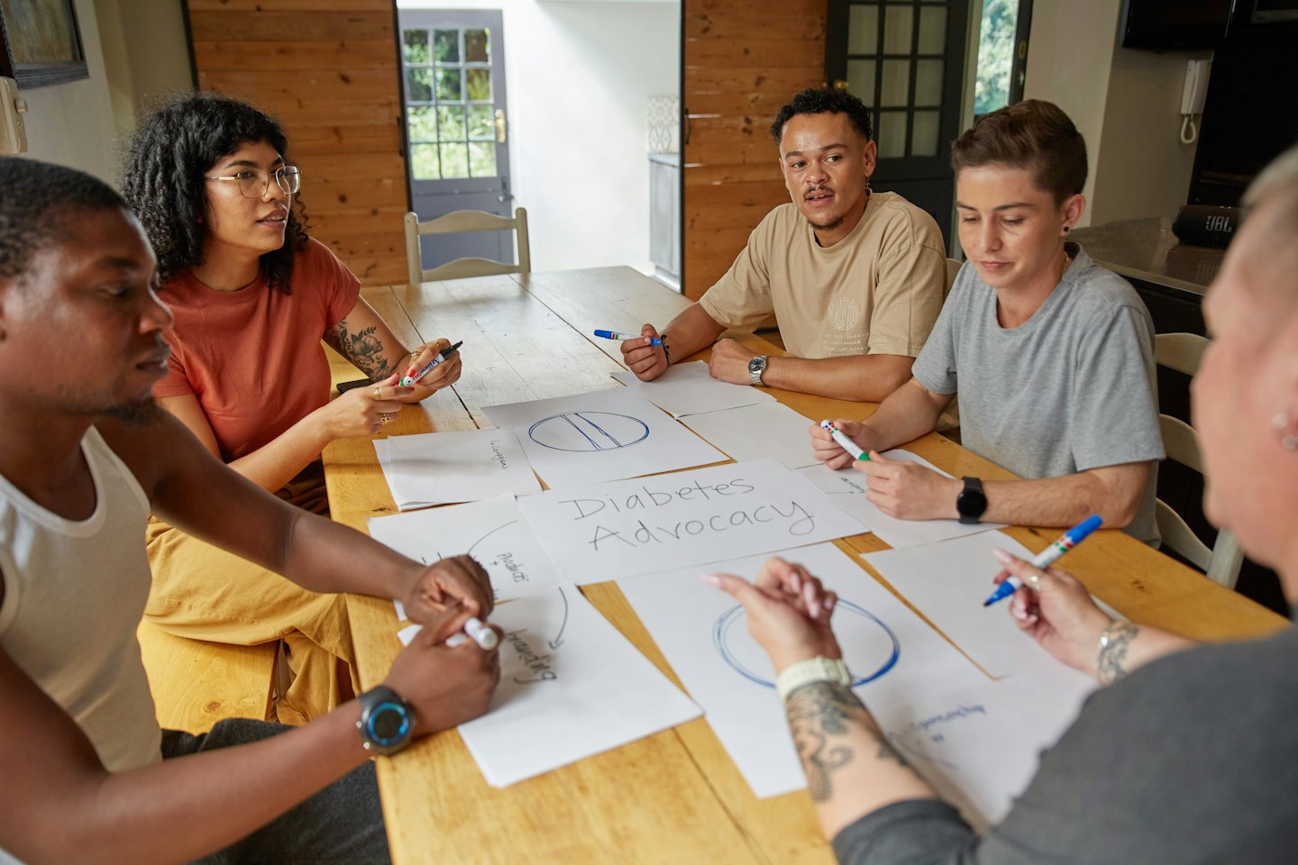 Diverse young adults brainstorm ideas around a table with markers.